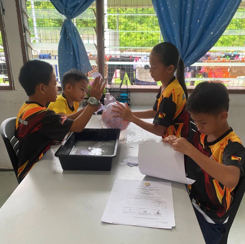 Eager young learners from SK Long Anap tearing recycled paper into pieces, the first step in creating their own papier-mâché globe.